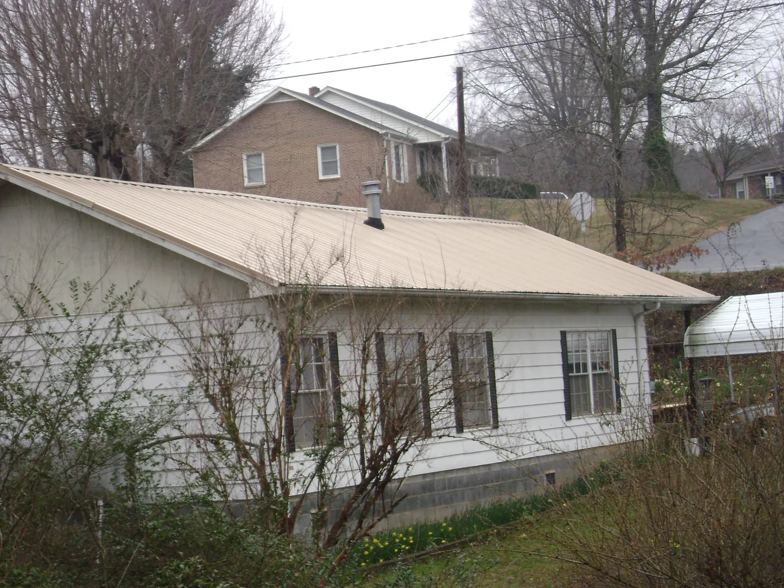 Tan metal roof on a white sided house set into a hillside — Commercial Roofing by Roofing Brothers in Belleville